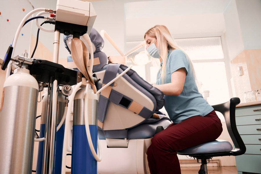 Side view of dentist treating kid teeth while child lying in dental chair. Equipment of inhalation sedation on foreground. Concept of children dentistry, stomatology and dental care.